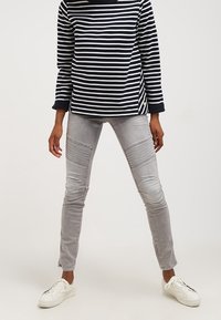Top de rayas marino y blanco de manga larga combinado con pantalones ajustados gris claro que presentan detalles acanalados y una textura suave. Zapatillas blancas completan el conjunto.