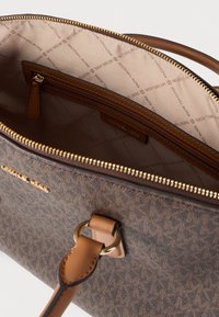 Καφέ τσάντα χειρός με μοτίβο, υφή στο εξωτερικό, φερμουάρ στην κορυφή και ταμπά εσωτερικό με εκτύπωση λογότυπου και μικρή τσέπη με φερμουάρ.