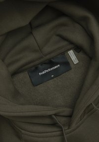 Felpa verde oliva con una morbida fodera interna. Presenta un'etichetta nera con "PeakPerformance" e la taglia "M". Polsini e orlo a coste.