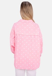 Rosa Langarmshirt aus strukturiertem, gekräuseltem Stoff mit weißen Herzmuster. Mit Rückenausschnitt und einer lockeren, übergroßen Passform.