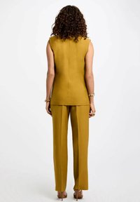 Top sin mangas color mostaza y pantalones a medida a juego, textura suave, diseño minimalista, acabado pulido, costuras sutilmente visibles.