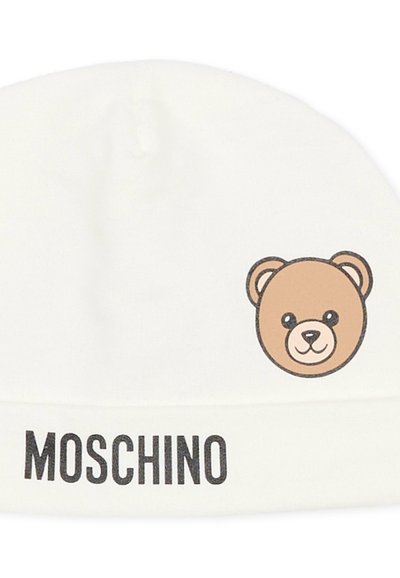 Gorro blanco de punto con un gráfico de cara de oso marrón y texto "MOSCHINO" en negro en la parte inferior. Material suave y tejido.