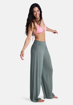 Haut de bikini triangle rose clair associé à un pantalon large fluide vert pâle, à taille smockée et texture douce.