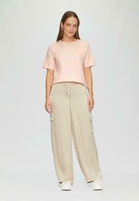 Jasnoróżowa bawełniana koszulka z krótkim rękawem i błyszczącym napisem, zestawiona z beżowymi spodniami cargo o szerokim kroju z bocznymi kieszeniami. Białe sneakersy.