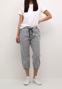 Pantalons capri rayés en bleu clair et blanc avec une taille élastique, fermeture à cordon de serrage et poignets élastiques ; associés à un t-shirt blanc uni.