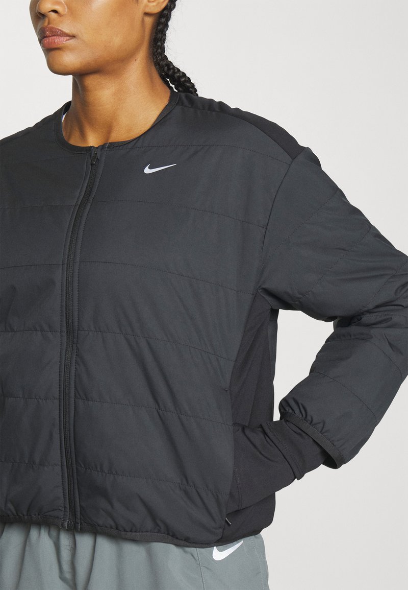Schwarze Daunenjacke mit Reißverschluss, gestepptem Design und elastischen Bündchen. Mit einem Nike-Logo auf der Brust und seitlichen Einsätzen aus einem kontrastierenden Material.