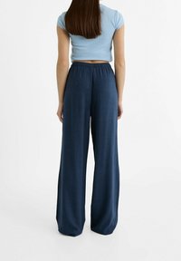 Granatowe spodnie typu wide-leg z elastycznym pasem, wykonane z lekkiego materiału. Charakteryzują się gładką fakturą i luźnym krojem.