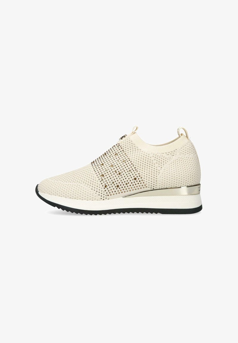 Beige stickad slip-on sneaker med metalliska nubb, dragflikar vid hälen och tungan, vit mellansula, svart zigzag yttersula och metallisk hälaccent.