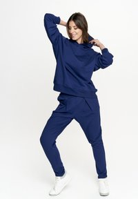 Granatowy sweatshirt i dopasowane joggersy z miękkiego materiału, z luźnym krojem i prążkowanymi mankietami. W zestawie z białymi sneakerami.