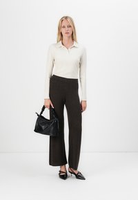 Ribbed cream long-sleeve polo shirt, dark brown wide-leg pants, black textured handbag, and black pointed-toe shoes with bow accents.
