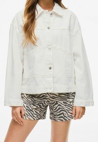 Vit denimjacka med avslappnad passform, med spetsig krage, framficka och silverfärgade tryckknappar, i kombination med shorts med zebramönster.