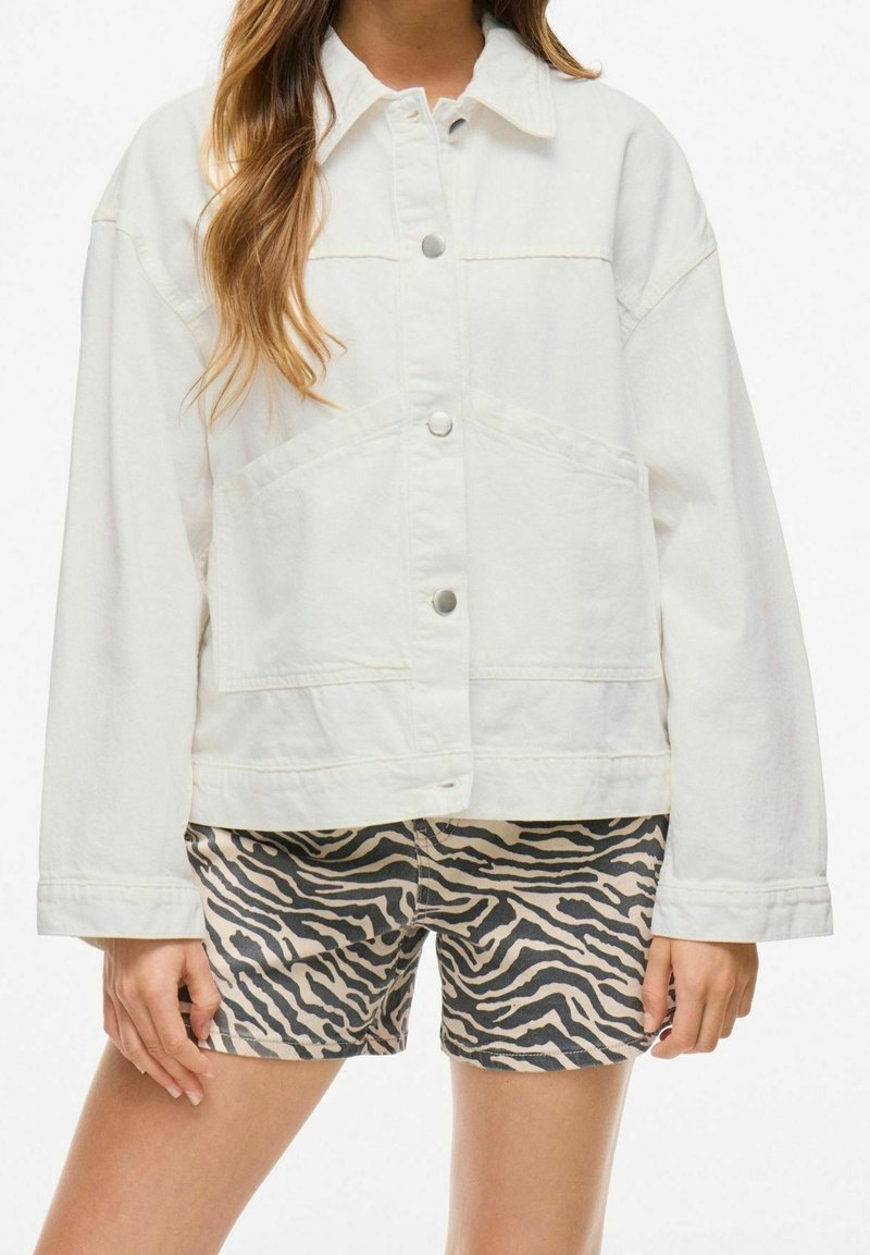 Vit denimjacka med avslappnad passform, med spetsig krage, framficka och silverfärgade tryckknappar, i kombination med shorts med zebramönster.