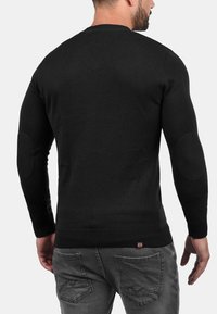 Maglione nero a maglia con maniche lunghe, scollatura rotonda, orlo a coste e toppe sui gomiti. Design aderente e texture liscia.