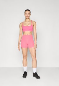 Rosa sports-bh med tynne stropper og matchende høyhælte shorts. Glatt tekstur med en tettsittende design. Svart treningstøy og hvite sokker.