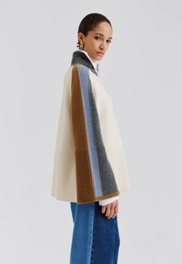 Pull coloré en blocs de crème, marron, gris et bleu ; avec une texture côtelée et un col haut ; coupe décontractée avec des manches larges.