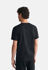 Camiseta de algodón negra con cuello redondo y mangas cortas. La vista trasera muestra una textura suave y un diseño minimalista, sin adornos.