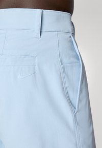 Világoskék Nike nadrág oldal- és hátsó zsebekkel, a jobb hátsó zseb közelében egy kis Nike swoosh logó található, amit egy személy visel.