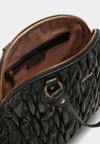 Zwarte gewatteerde handtas met goudkleurige accenten, een ritssluiting en een gladde binnenvoering. Voorzien van een binnenvak voor organisatie.