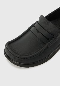 Loafer din piele neagră cu finisaj texturat, având detalii cusute și o bandă superioară proeminentă. Design minimalistic cu vârf rotunjit.
