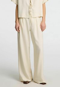 Lys beige to-delt outfit med en kortærmet top med knydeafbryder og vide bukser. Blødt, glat stof med minimalt design.