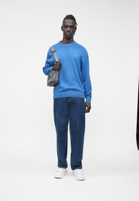 Modra jopa, kavbojke iz jeansa in bele superge. Siva torba, sproščen kroj, gladka tekstura in rebrasti manšeti na puloverju.