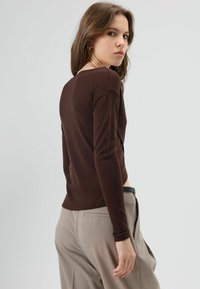 Bruine geribbelde top met lange mouwen, voorzien van een ronde halslijn en een aansluitend model, gecombineerd met beige broek met hoge taille en een zwarte riem.