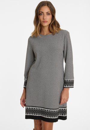 Black and white long-sleeve dress featuring a houndstooth pattern, embellished cuffs, and a patterned hemline. Smooth fabric texture.