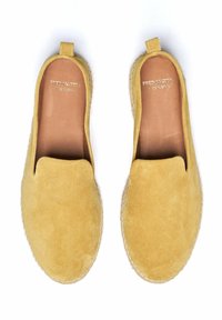 Zapatos de ante amarillos tipo slip-on con suela plana, que cuentan con una entresuela de yute cosida y un pequeño lazo en el talón. Fabricados en España.