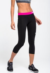 Czarne legginsy capri z różowym pasem, wykonane z elastycznego materiału. Posiadają białe logo Nike na dolnej części lewej nogawki. Krój dopasowany do sylwetki.