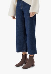 Kvinna klädd i vida blå denimjeans, krämfärgad fluffig tröja och bruna mockakängor med blockklackar och sidoglädsel.