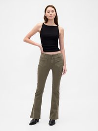 Débardeur noir ajusté à bretelles larges, associé à un pantalon évasé vert olive avec poches arrière et tissu texturé. Bottines noires à talons.