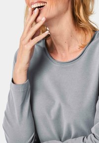 Graues Langarmshirt mit Rundhalsausschnitt, aus weichem Material gefertigt; hat eine lockere Passform und sichtbare Nähte entlang der Nähte.