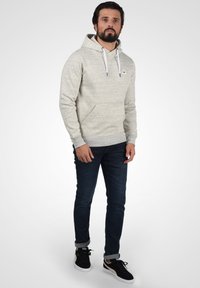 Lichtgrijze hoodie met een gestructureerde afwerking, verstelbare koordjes en een voorzak. Gecombineerd met donkerblauwe jeans en zwarte sneakers.