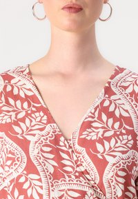 Red floral-patterned dress with a v-neckline, featuring white botanical designs. Soft fabric with a lightweight texture, enhanced by hoop earrings.