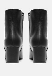 Bottines en cuir noir avec un talon carré et des fermetures éclair sur le côté. Présente une texture lisse et des détails de couture précis.