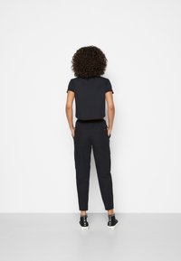 Svart kortärmad t-shirt i kombination med tapered svarta cargobyxor. Plaggen har en enkel design, slitstarkt material och en avslappnad passform.