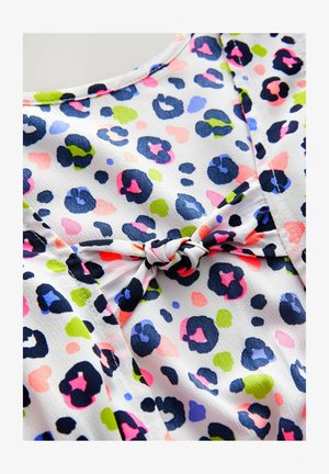 Bela tkanina s večbarvnim odtisom leoparda, z modrimi, roza, zelenimi in črnimi lisami. Središnja mašna podrobnost dodaja teksturo.