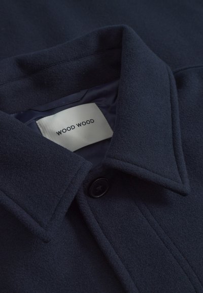Navy blue wool coat with a structured collar, featuring a button closure and a satin inner lining. Label reads "WOOD WOOD."