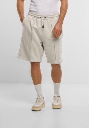 Helle beigefarbene Baumwollshorts mit Seitentaschen, Kordelzugbund und umgeschlagenen Säumen, kombiniert mit weißen Kniestrümpfen und Sneakers.