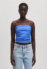 Strapless blauwe top van rekbaar materiaal, met gathered textuur op het lichaam, gecombineerd met lichtblauwe high-waisted jeans.