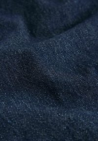 Tmavomodrý denimový materiál so hladkou textúrou, ktorý má jemné vertikálne pruhy a mierny lesk.