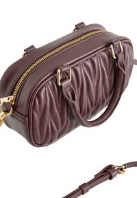 Vadderad bordeauxfärgad läderhandväska med gulddragkedja, dubbla topphandtag och avtagbar axelrem. Mjuk textur och polerade metalldetaljer.