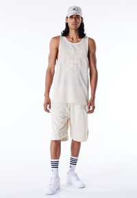 Lyse beige mesh sportstopp med "20" trykk, kombinert med matchende shorts. Hvite joggesko og sortstripete ankelsokker fullfører stilen.