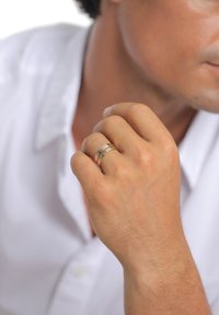 Käel kantavad hõbe- ja kuldsõrmused, millel on siledad ja tekstuuriga mustrid, sõrmus on sõrmeindeksil, valge särgi taustal.