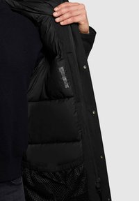 Melnā pūkainā jaka ar rāvējslēdzēju priekšpusē, ar gludu ārpusi un sišanas iekšpusi. Tajā ir acu kabata un aprūpes etiķete.