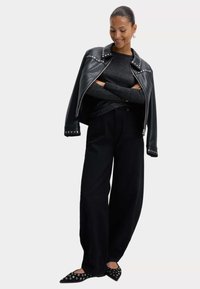 Schwarze Leder-Motorradjacke mit silbernen Nieten, kombiniert mit einem dunklen Pullover, weiten schwarzen Hosen und spitzen schwarzen Schuhen mit Ösenakzenten.