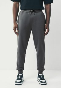 Gray jogger pants with elastic waistband and drawstring. Soft fabric, tapered design, side pockets, paired with black and white sneakers.