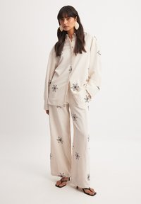 Linnen shirt en wijde broek set in roomkleur, met zwarte bloemen borduursels. Comfortabele pasvorm met een knoopsluiting en geaccentueerde kraag.