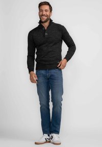 Donkergrijze gebreide trui met een kraag met halve knopen, geribbelde manchetten en zoom, gecombineerd met blauwe denim jeans en witte sneakers met zwarte strepen.