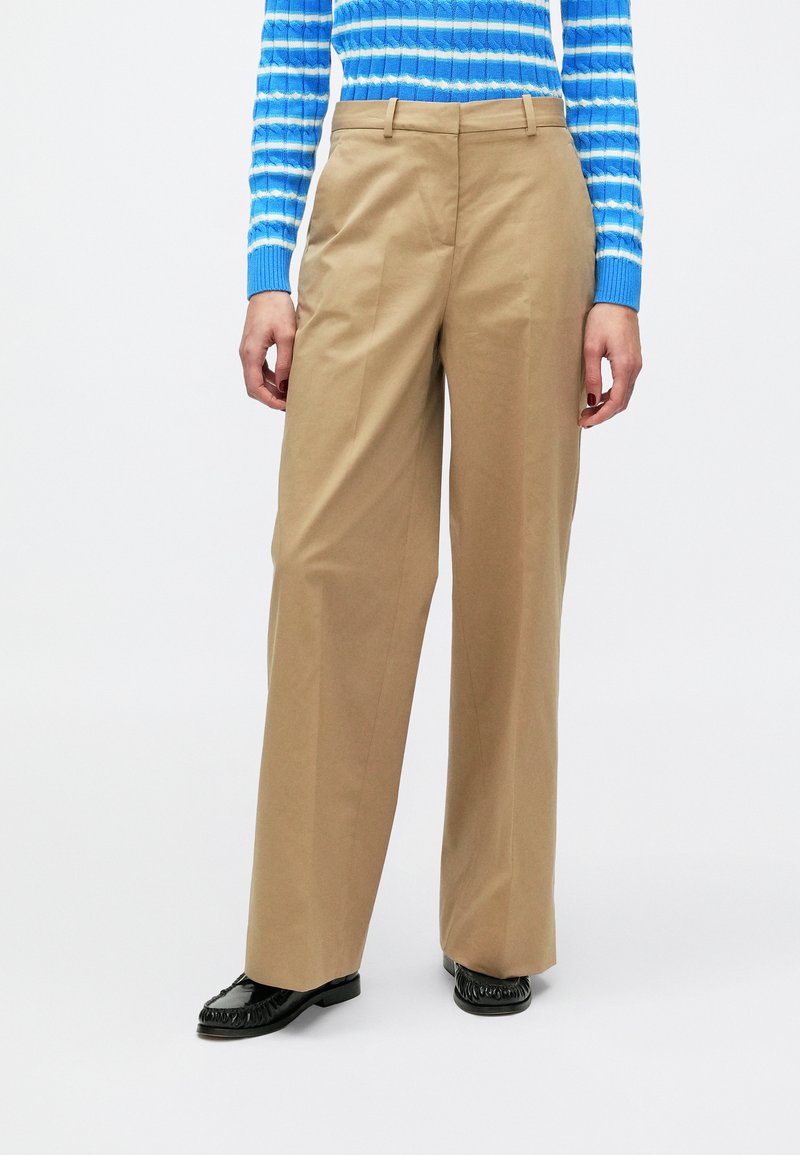 Μπεζ παντελόνια με φαρδιά μπατζάκια και ομαλή υφή, διαθέτουν θηλιές για ζώνη και καλοραμμένη εφαρμογή. Συνδυασμένα με μαύρα μοκασίνια στα πόδια.